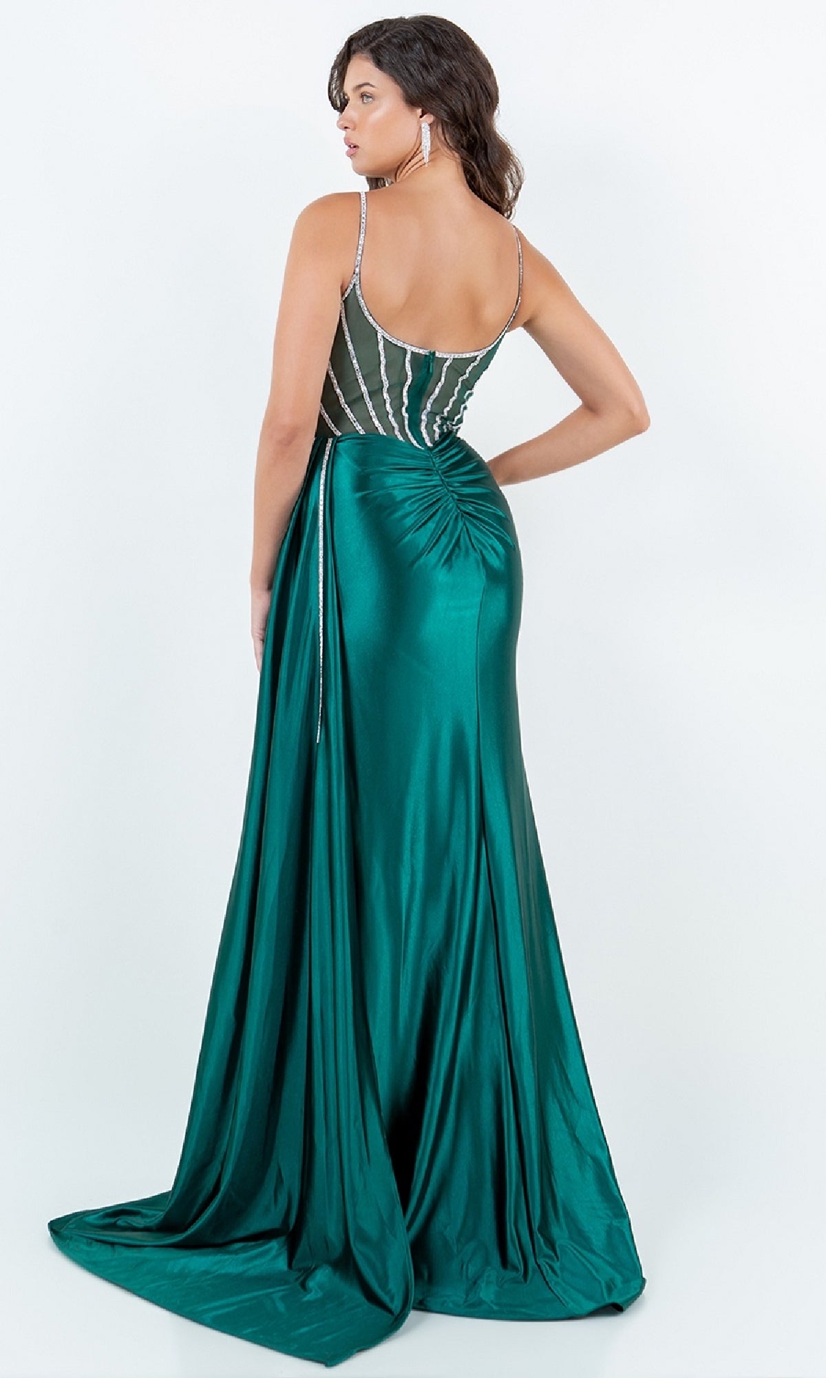 A woman faces away from the camera wearing the Cinderella Couture 8219J Side-Sash Long Prom Gown, a plus size, floor-length emerald green satin dress with a ruched back and sheer bodice.